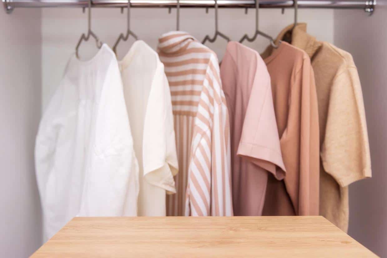 Stylist fashion wardrobe in neutral beige tones. Mockup for washing powder or bleach. Copy and paste space for text or your product. In the foreground is an empty, wooden table for product placement.