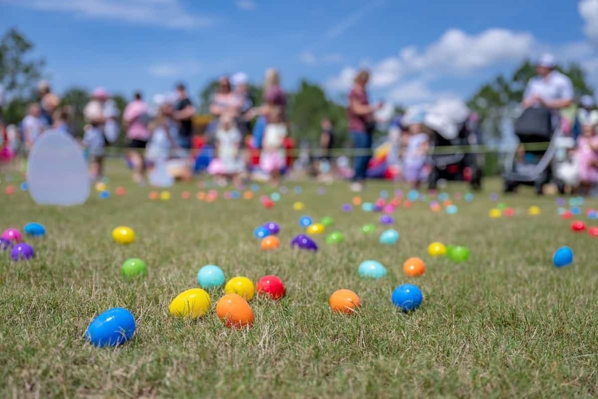 Colorful eggs scattered on grass with people in the background at an outdoor event, likely enjoying after Easter sales.