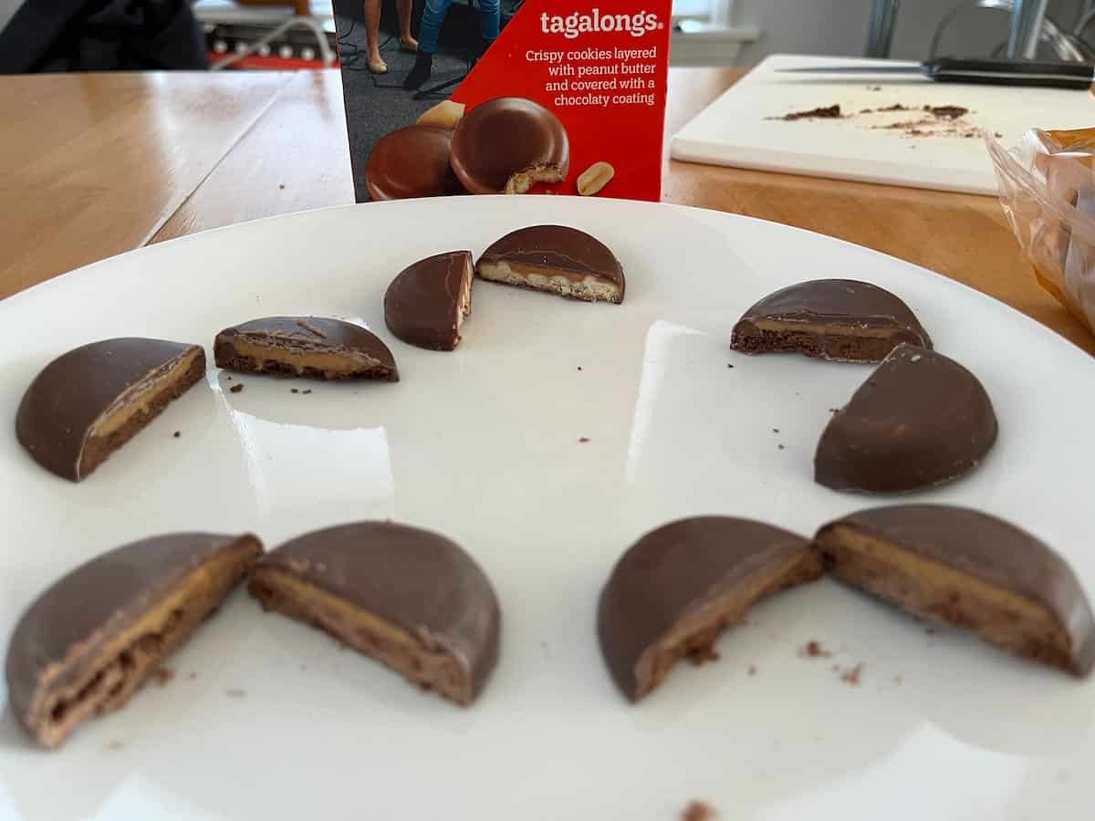 A plate of chocolate-coated generic Girl Scout cookies, some cut in half to reveal a layered filling, on a table with a cookie box in the background.