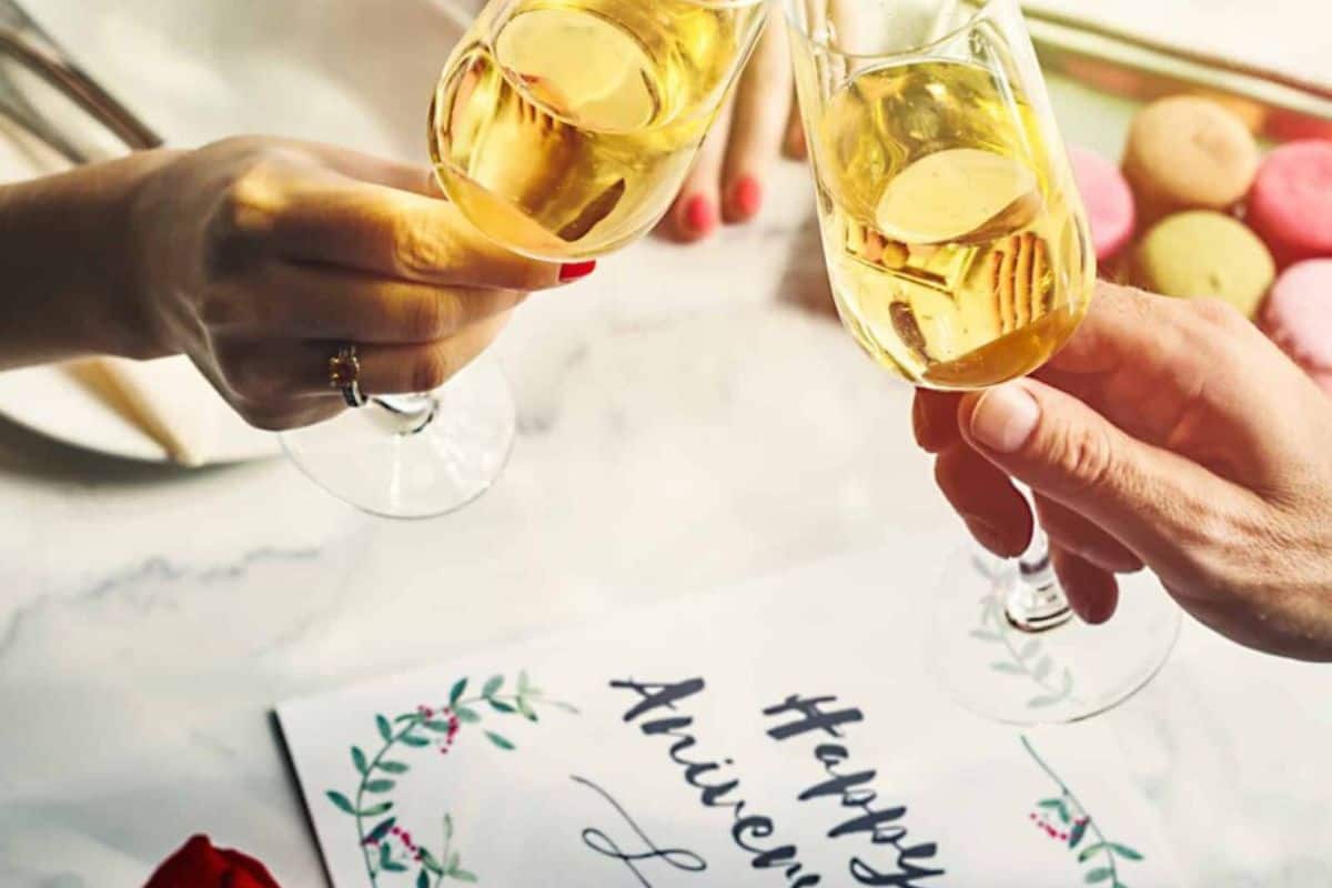 Couple clinking champagne glasses over card that reads happy anniversary.
